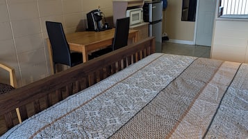 A room with a bed, a desk, a chair, a microwave, a refrigerator, and a door leading to a balcony.