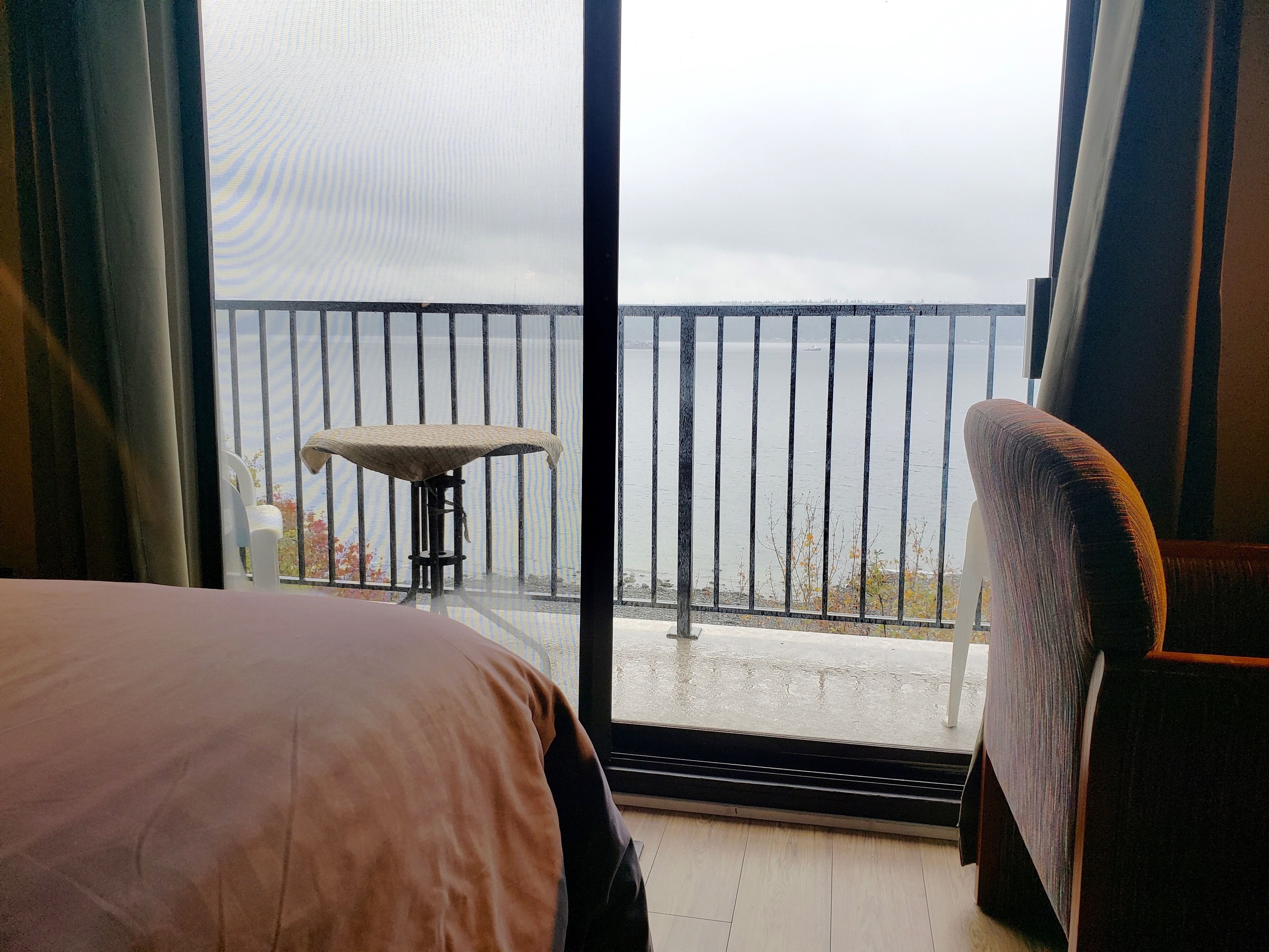 A room with a bed, a chair, and a balcony with a railing.