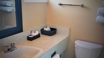 A bathroom with a sink, mirror, towel rack, toilet, and a window.