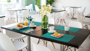 Ein moderner Essbereich mit Tischen, Stühlen und einem Mittelstück aus einer Glasvase mit Blumen und Früchten.
