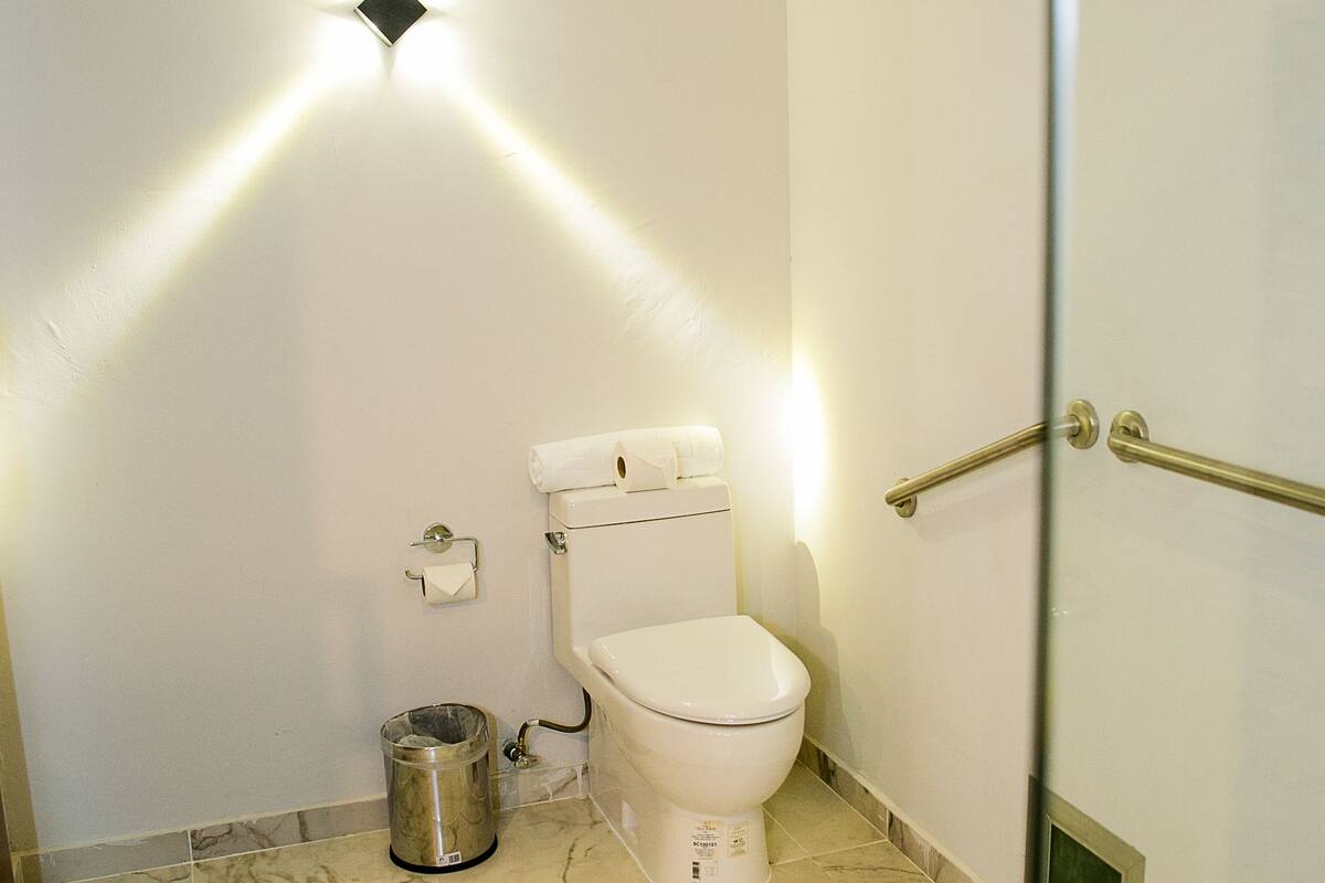 Un baño con inodoro, un cubo de basura y una puerta de ducha de cristal.
