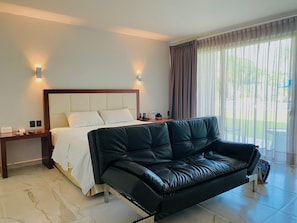 A hotel room with a bed, a black leather sofa, a nightstand, and a window with curtains.