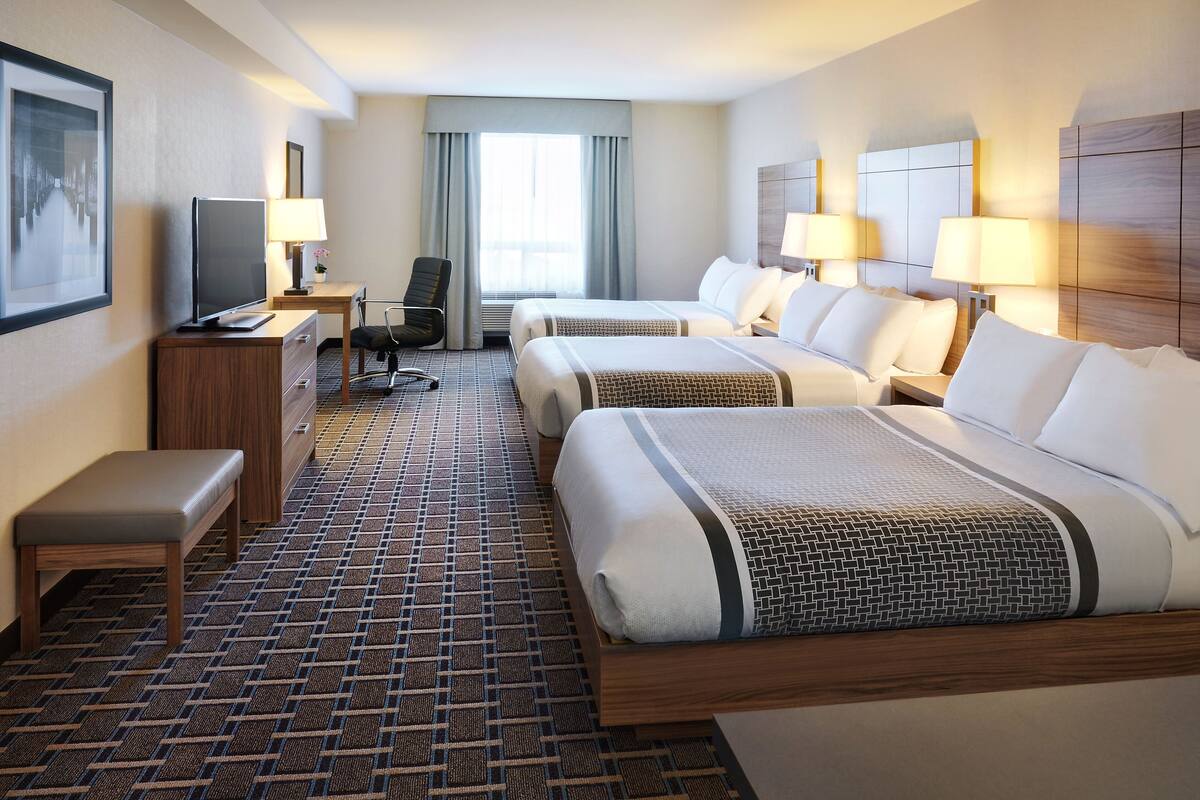 A hotel room with two beds, a desk with a computer, a chair, and a bench.