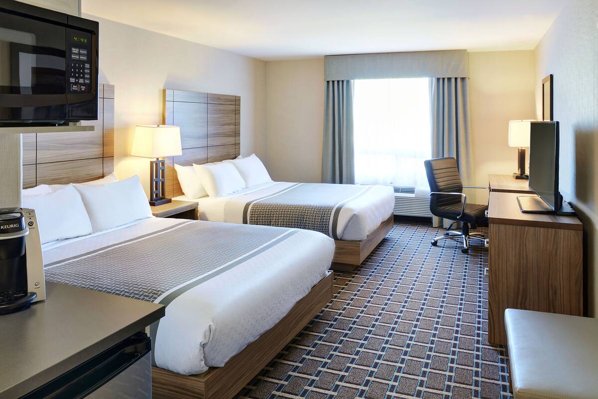 A hotel room with two beds, a desk with a computer, a microwave, and a coffee maker.