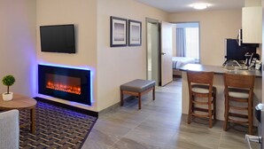 A modern hotel room with a fireplace, a flat-screen TV, a small dining area, and a kitchenette. - Pomeroy Inn And Suites Vermilion (Vermilion)