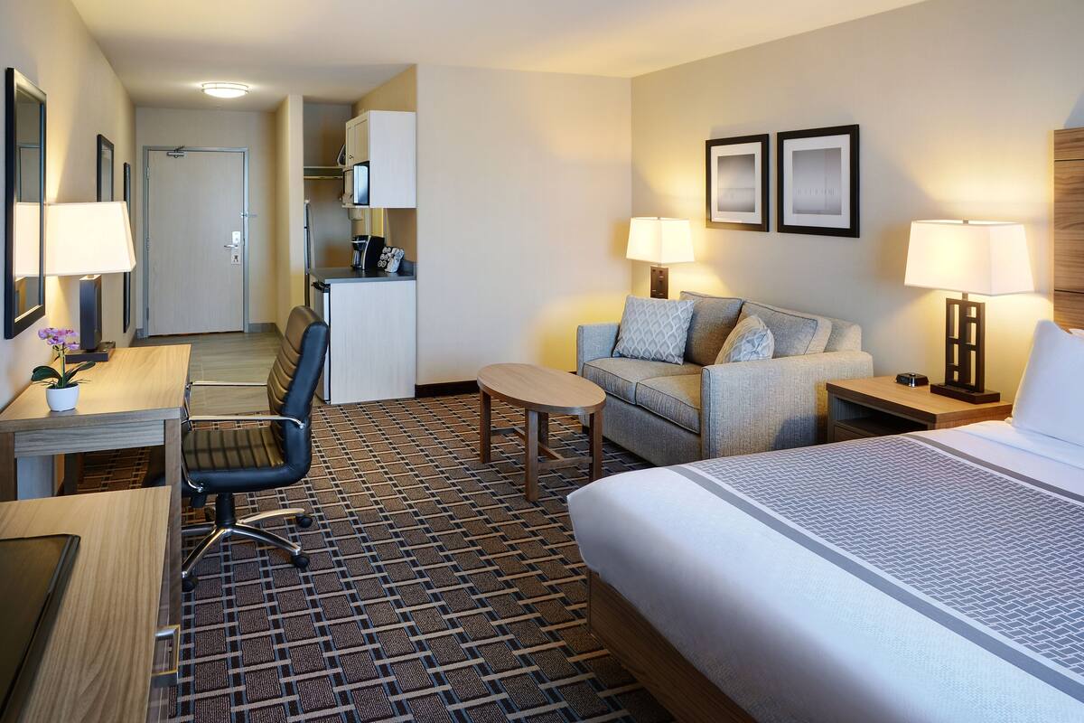 A hotel room with a bed, a desk, a chair, a sofa, and a small table.