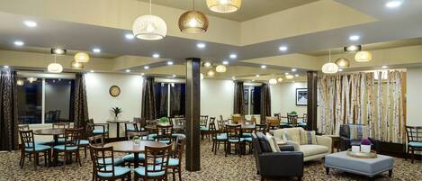 A hotel lobby with multiple dining tables, chairs, and a seating area with sofas and an ottoman.