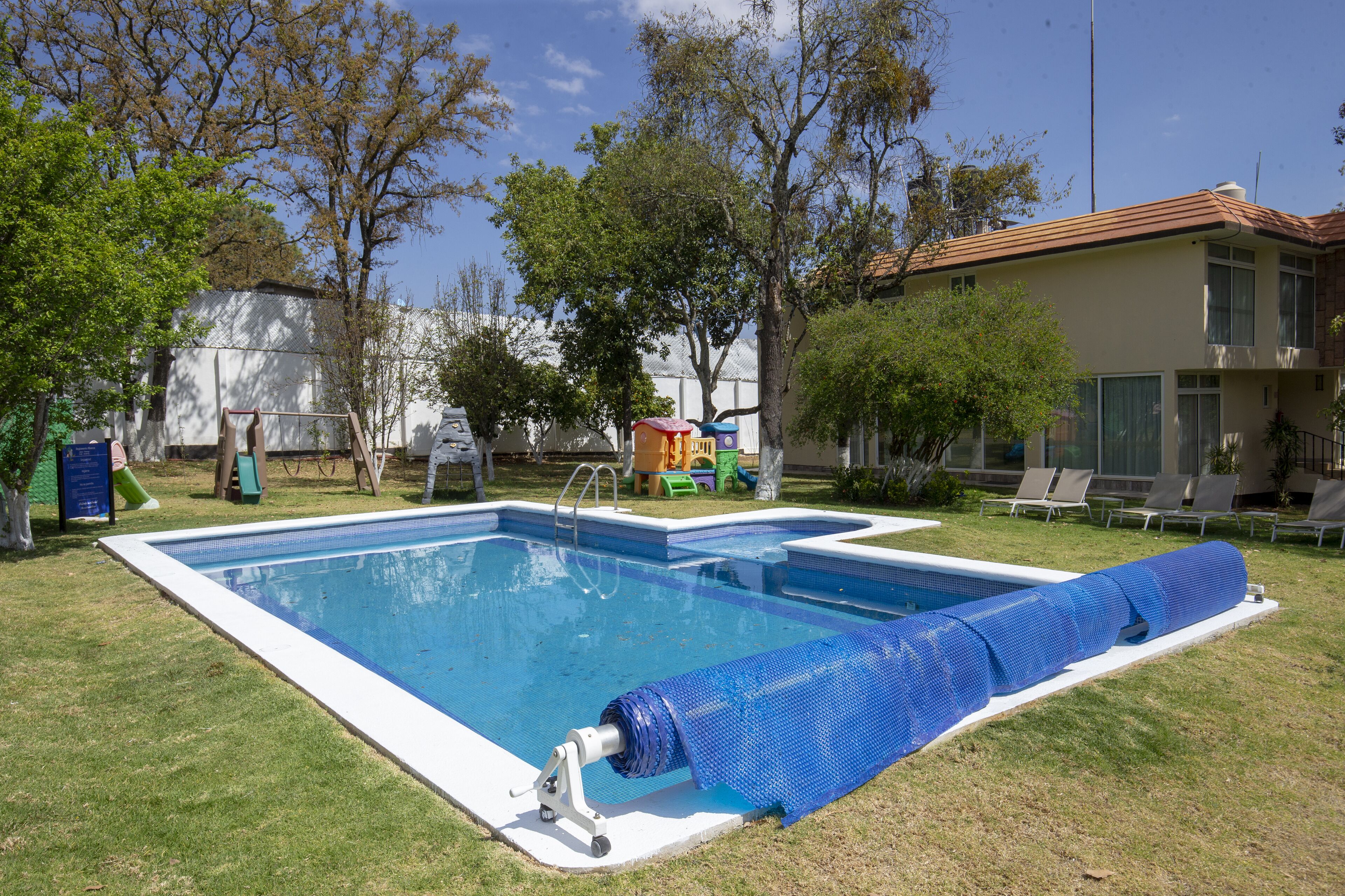 A rectangular swimming pool with a blue cover, surrounded by a grassy lawn and trees.