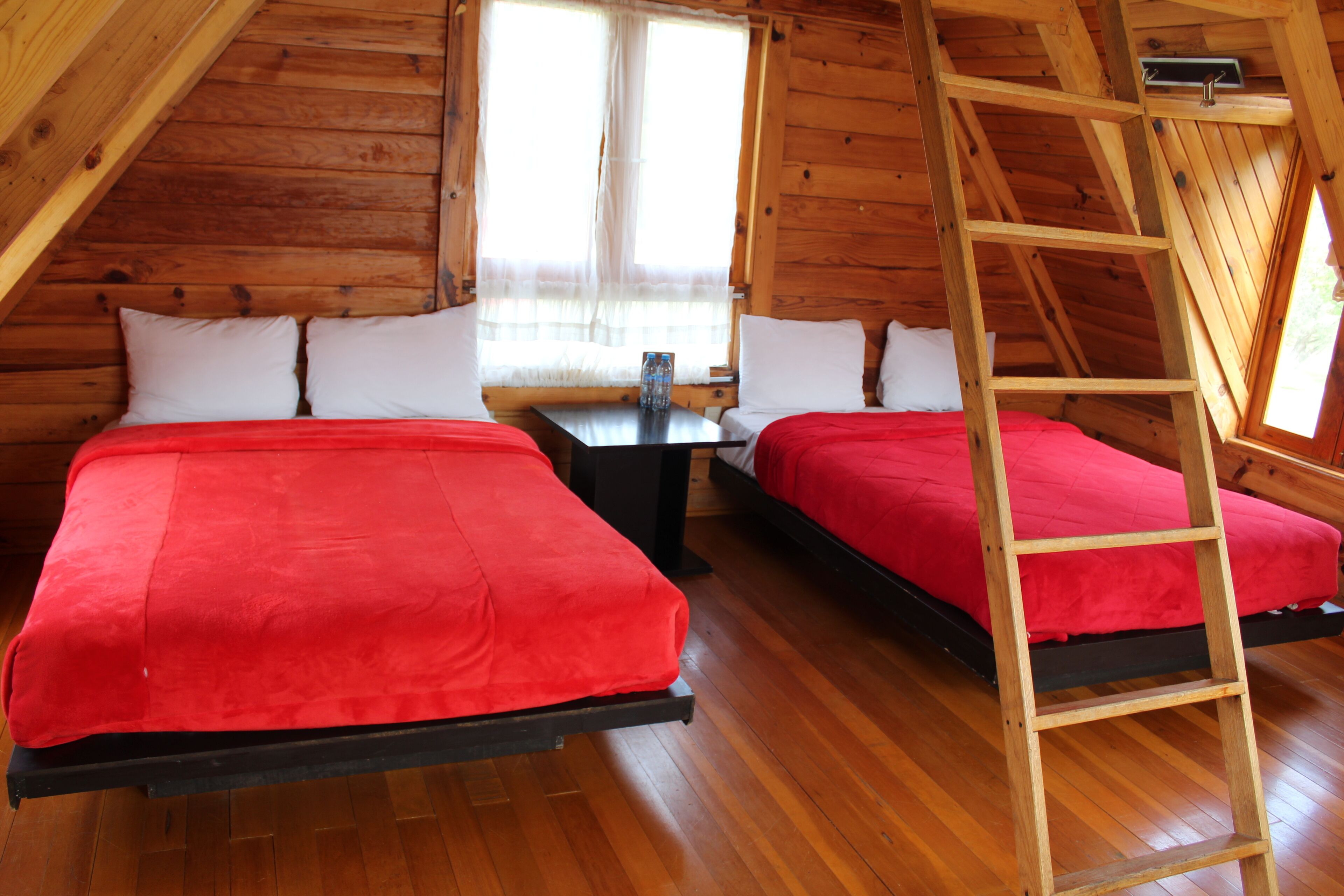 A cabin with two beds, wooden floors, a table with a bottle, and a ladder.
