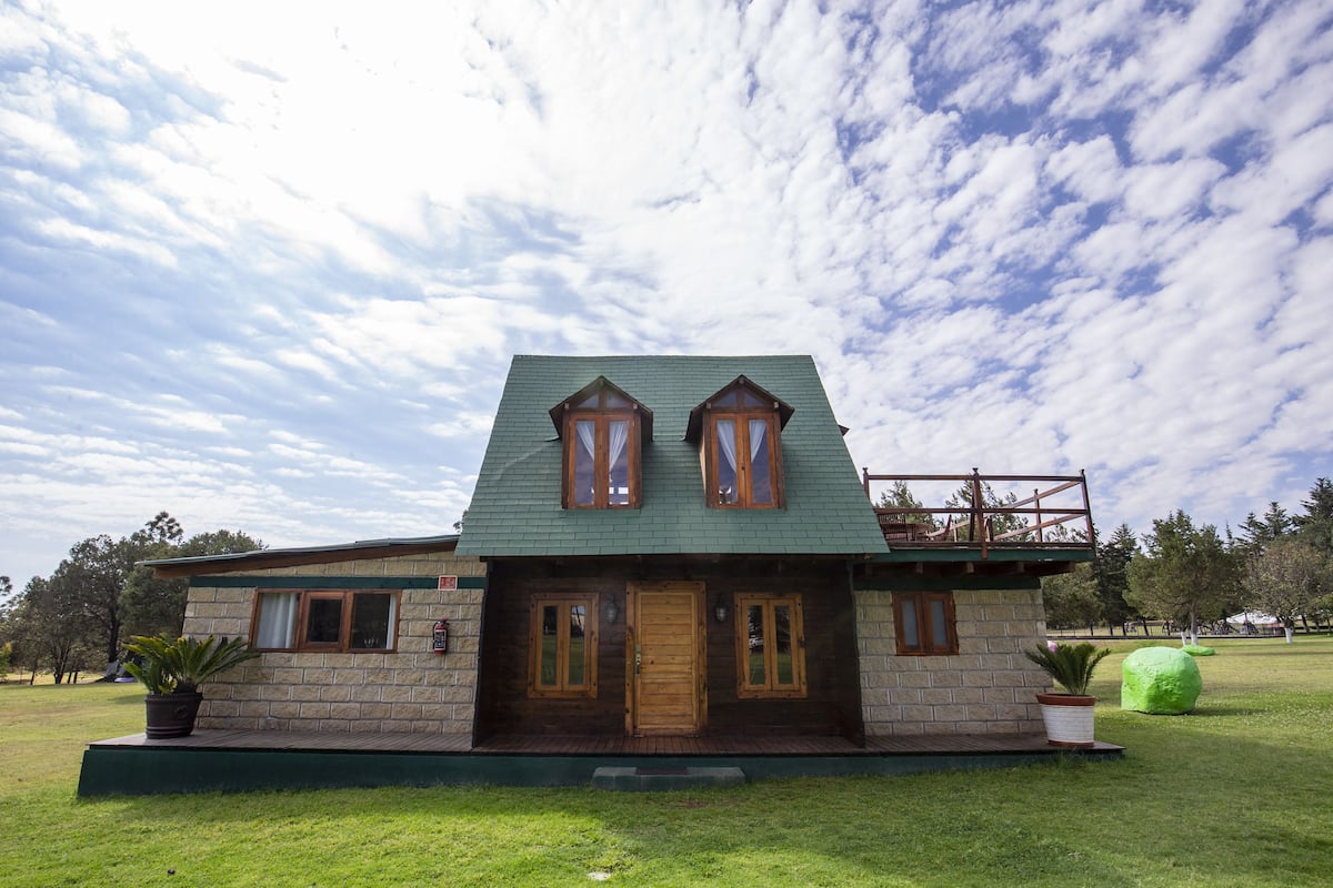 A two-story house with a green roof, wooden windows, and a small balcony.
