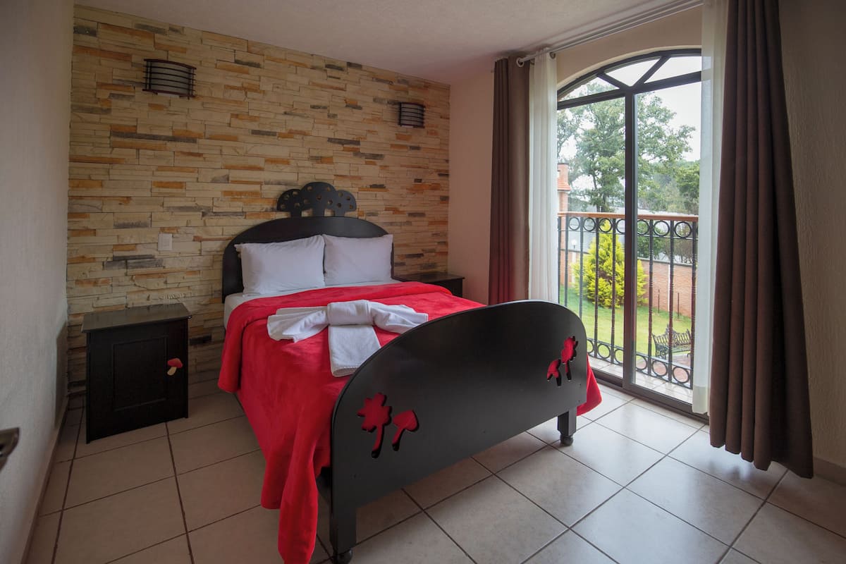 A bedroom with a bed, a nightstand, a window with curtains, and a stone-patterned wall.