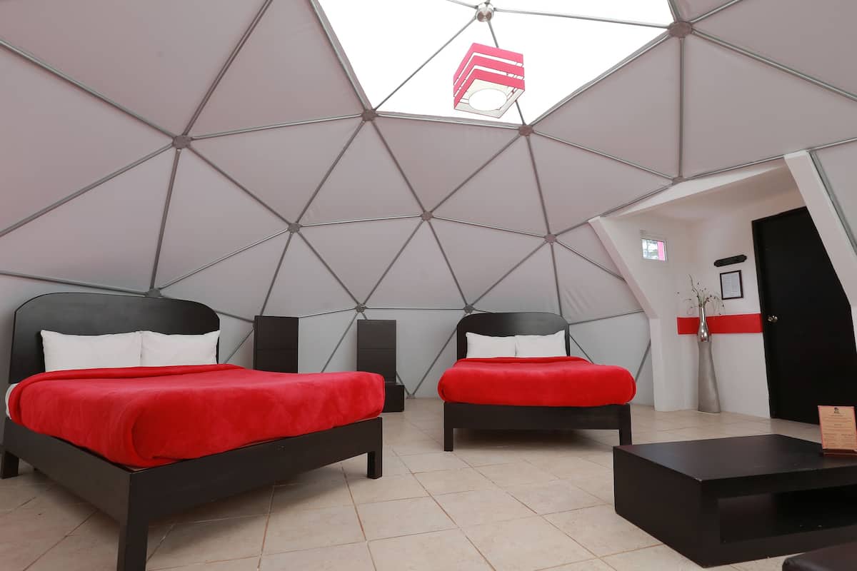 A modern room with two beds, a small table, and a ceiling with a geometric design.