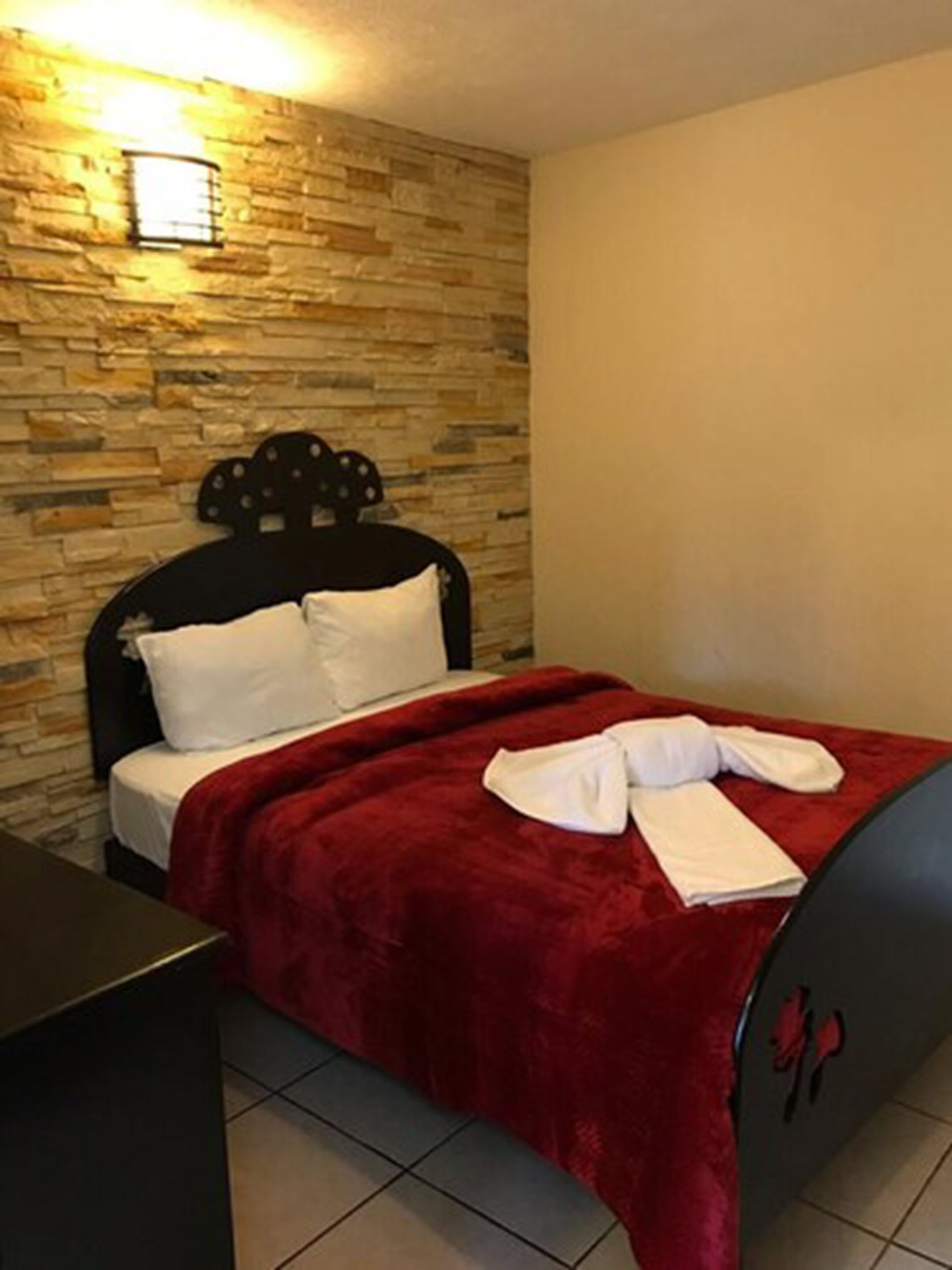 A bed with a red blanket, white pillows, and a neatly folded towel on the side.