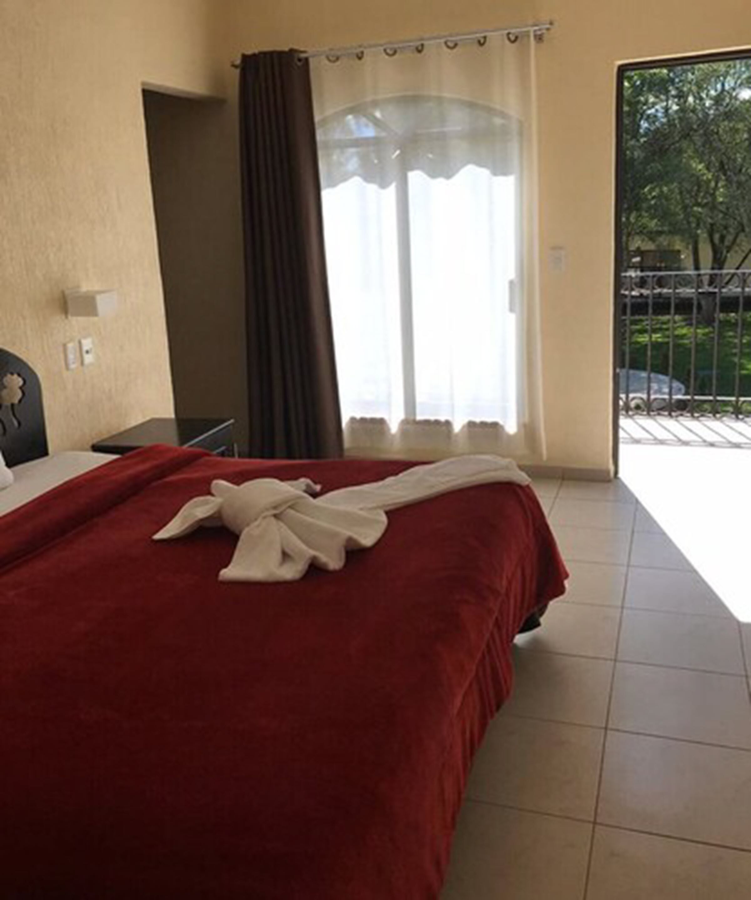 Ein Hotelzimmer mit einem großen Bett, Blick ins Freie durch eine Schiebetür und ein Balkon mit Metallgeländer.