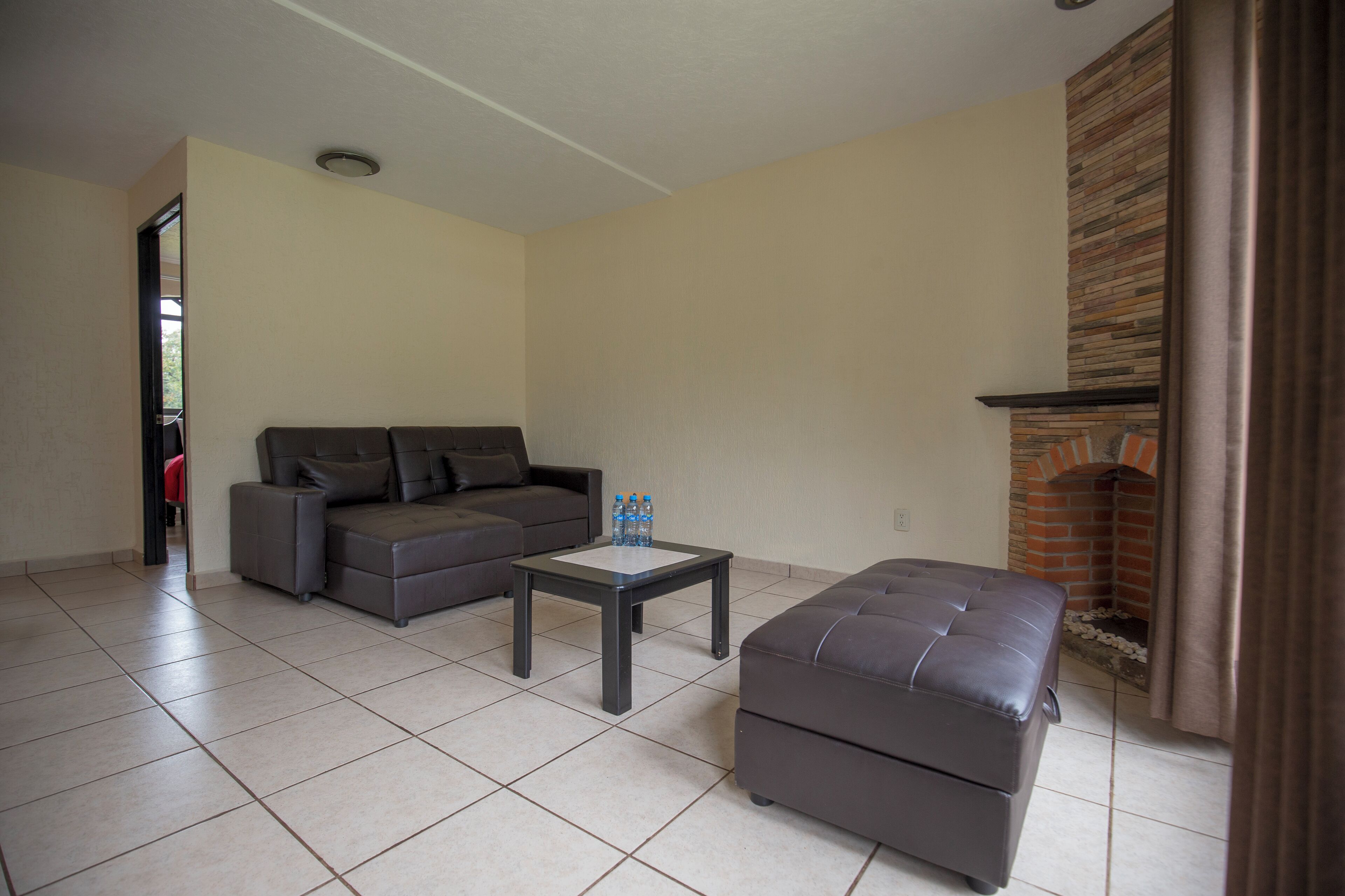 A living room with a sofa, ottoman, and a coffee table. There is a fireplace with a stone facade.