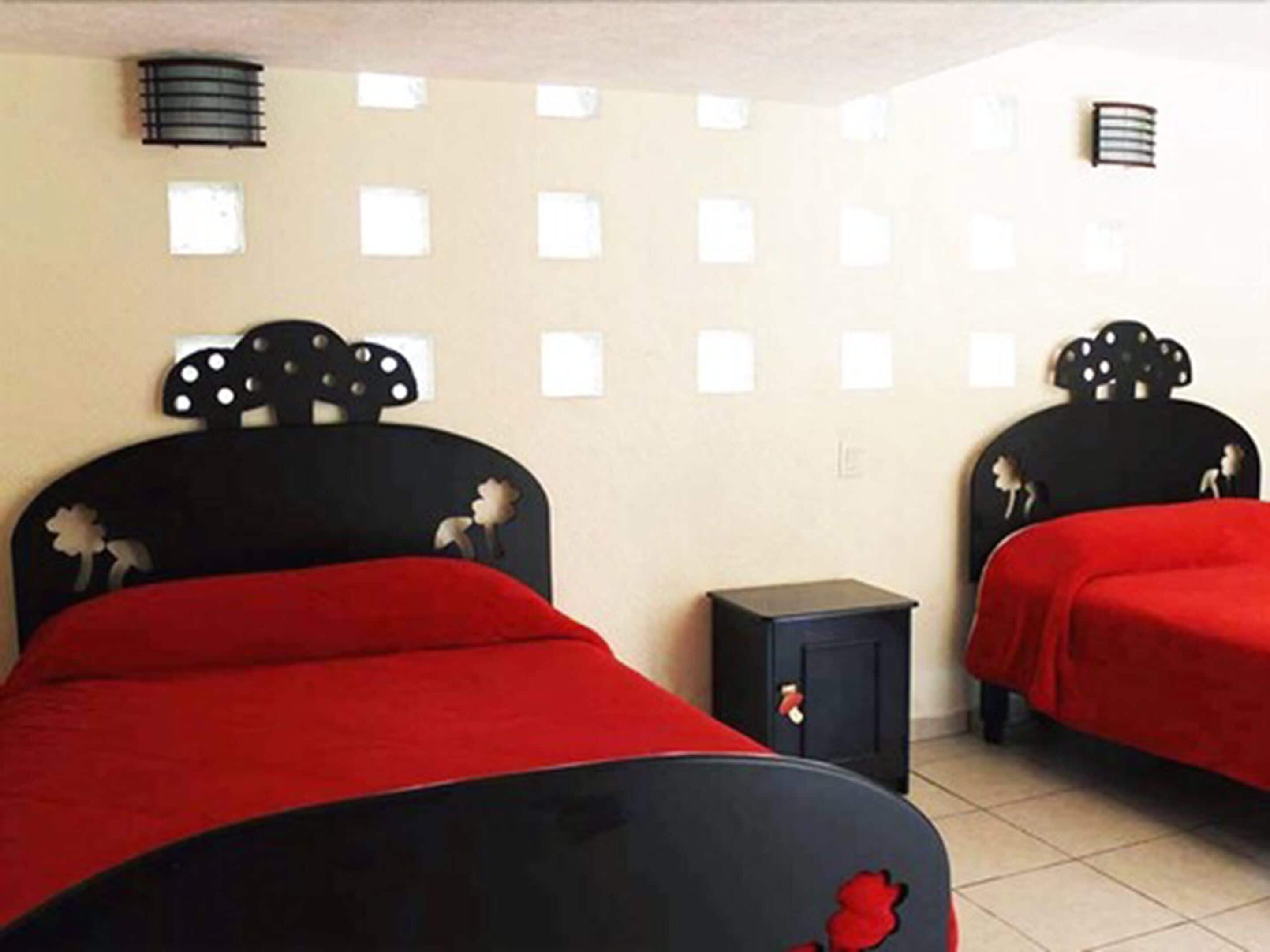 Une chambre d’hôtel avec deux lits, chacun doté d’une tête de lit noire et d’une literie rouge. Une petite table de chevet noire se trouve entre les deux lits.