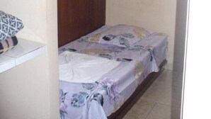 Una habitación pequeña con una cama individual, cabecera de madera, ropa de cama estampada con motivos florales, un armario blanco y una ventana con cortina.