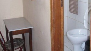 Un baño pequeño con inodoro, estante de madera, silla y mesa.