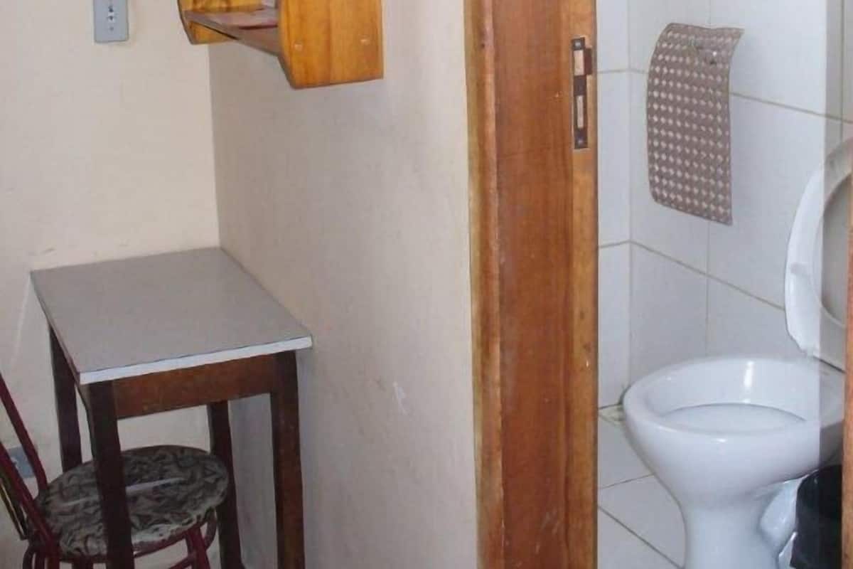 Un baño pequeño con inodoro, estante de madera, silla y mesa.