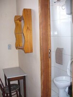 Un baño pequeño con inodoro, estante de madera, silla y mesa.