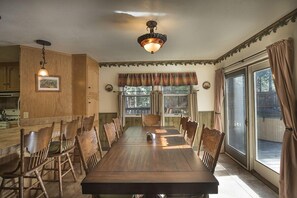 A dining room with a long wooden table, chairs, a chandelier, and a view through a window with curtains. - Yosemite Scenic Wonders - Wawona Area (Yosemite National Park)