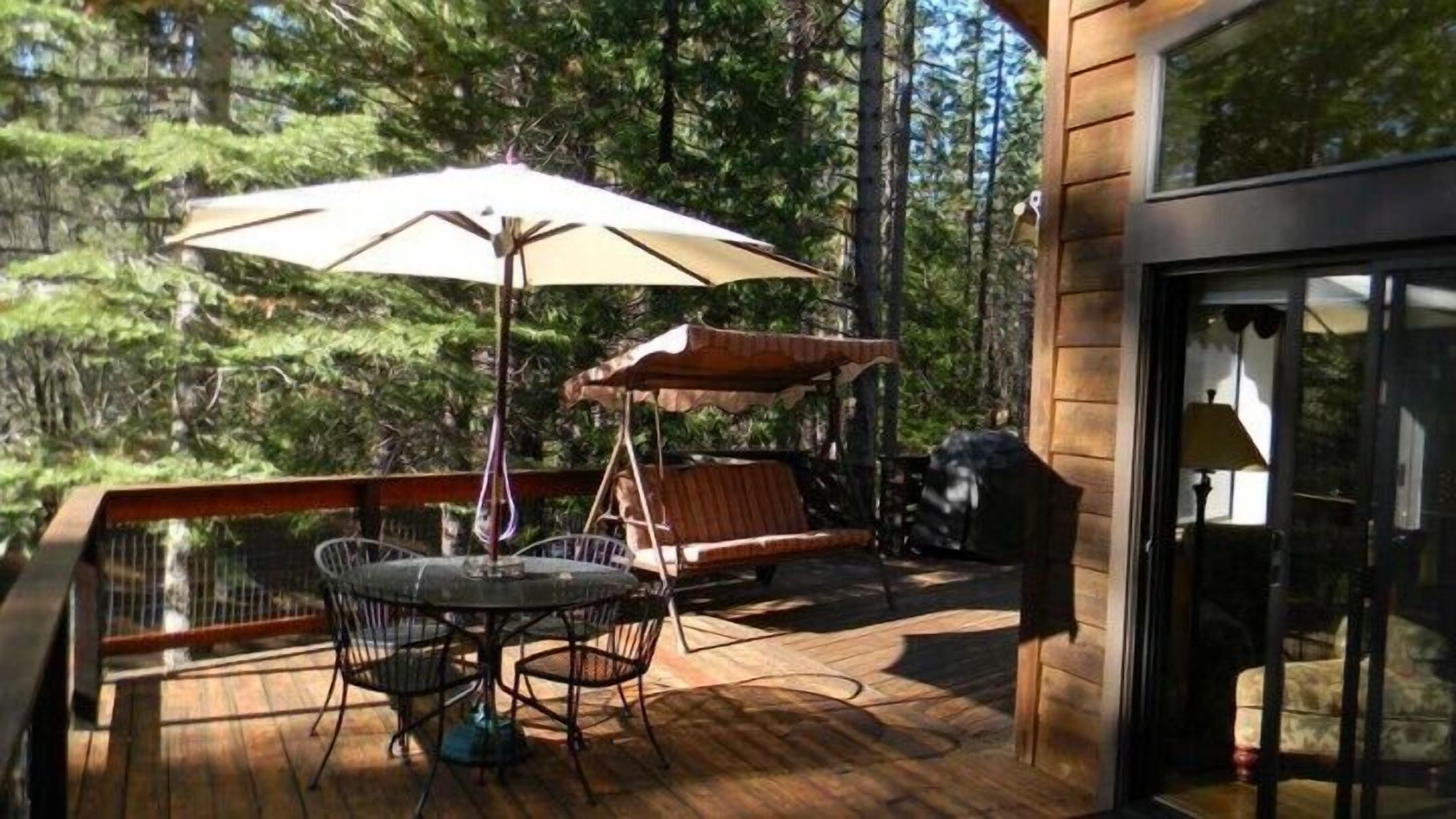 A wooden deck with a table and chairs, a hanging chair, and a large umbrella.