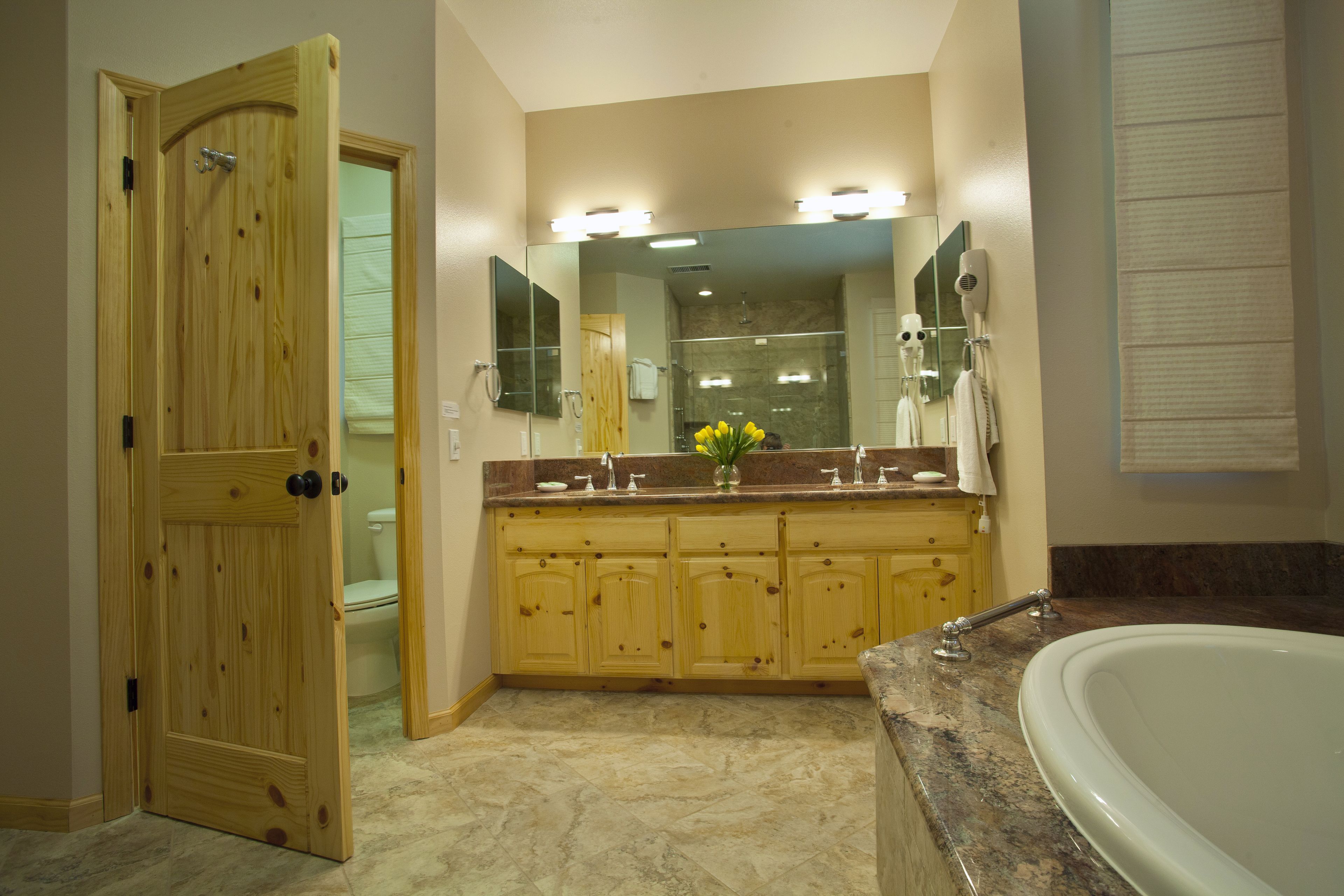 A bathroom with a wooden door, a large mirror, a vanity with a sink, and a bathtub.