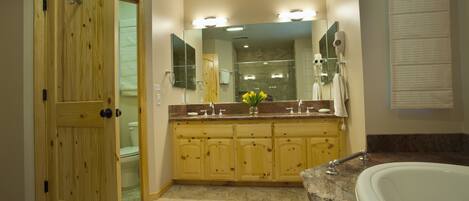 A bathroom with a wooden door, a large mirror, a vanity with a sink, and a bathtub.