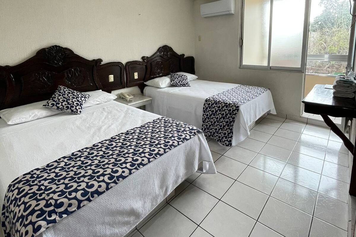 Habitación de hotel con dos camas, ventilador de techo, aire acondicionado y ventana con vistas.
