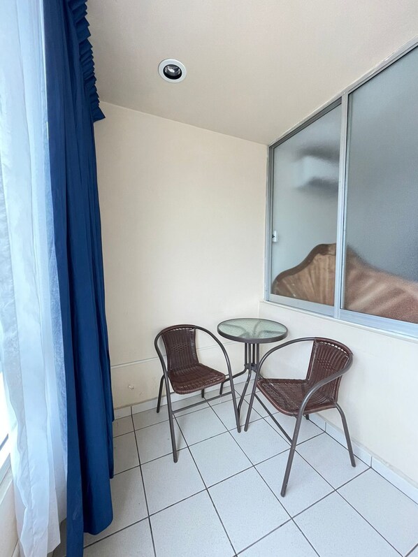 A small balcony with two wicker chairs and a glass table, a window with a view, and a ceiling light. - Hotel California (Tuxpan)