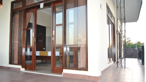 A building entrance with a sliding glass door, a tiled floor, and a balcony with a metal railing. - Ganesha Home Stay (Ubud)