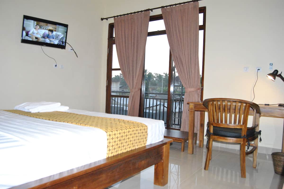 A hotel room with a bed, a desk, a chair, and a TV mounted on the wall.