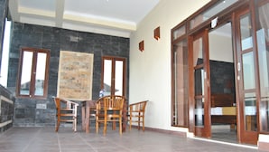 A spacious room with a tiled floor, a wooden table with chairs, a large window, and a sliding glass door leading to a bedroom. - Ganesha Home Stay (Ubud)