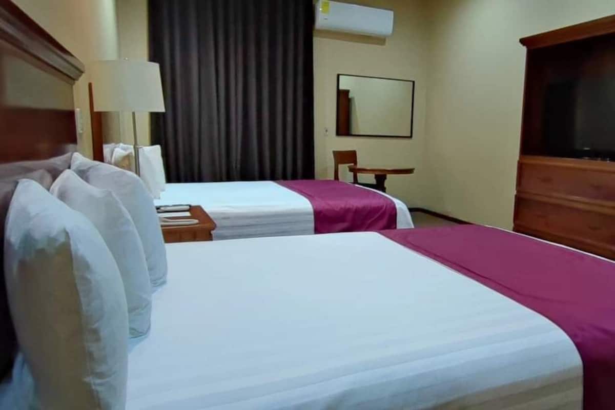 A hotel room with two beds, a desk, a chair, a television, and a wardrobe.