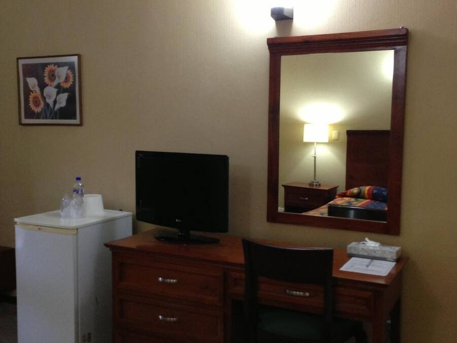 Habitació d'hotel amb escriptori, televisió, tauleig, mirall i llit amb manta colorida.