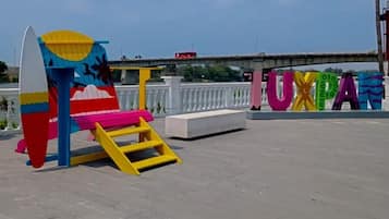 Relax in a vibrant outdoor seating area with a surfboard-shaped bench and ladder, overlooking a scenic waterfront or bridge.