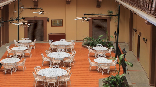 An outdoor patio with multiple white tables and chairs, a central fountain, and terracotta pots.