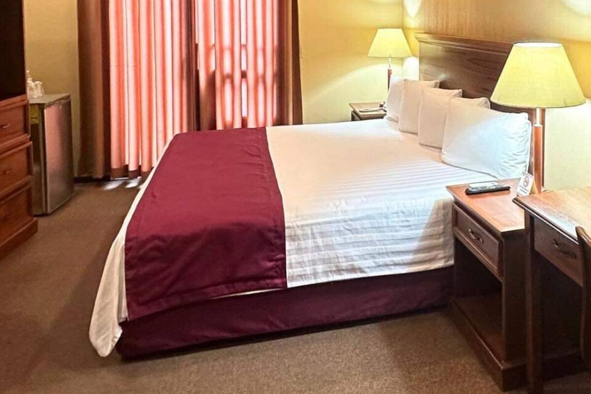 A hotel room with a large bed, a wooden dresser, a TV, and two bedside lamps.