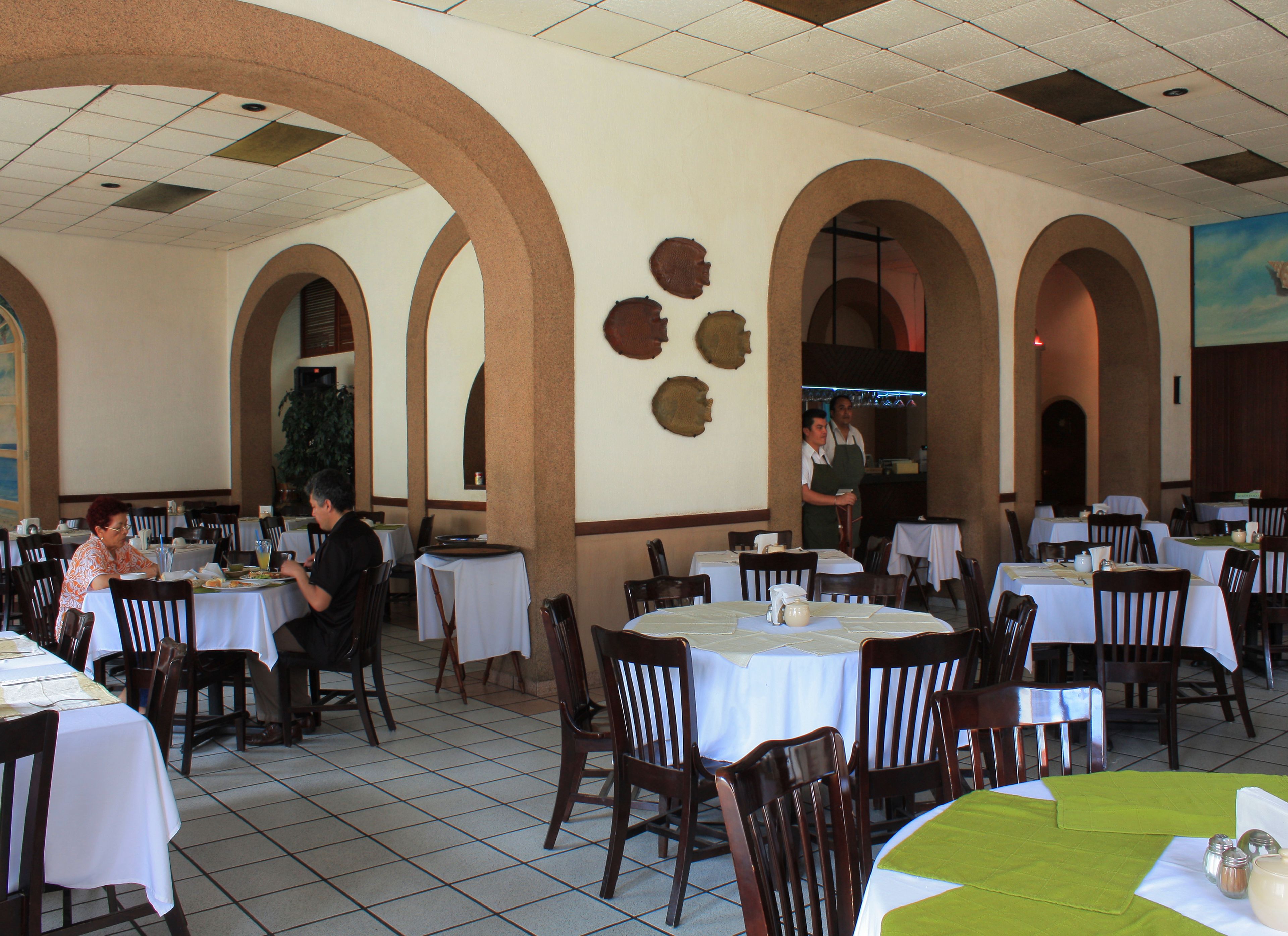 A restaurant with multiple tables and chairs, a tiled floor, and a ceiling with recessed lighting.