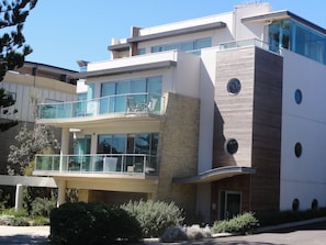 A modern multi-story hotel with glass balconies, a stone facade, and a clear view of the surrounding area.