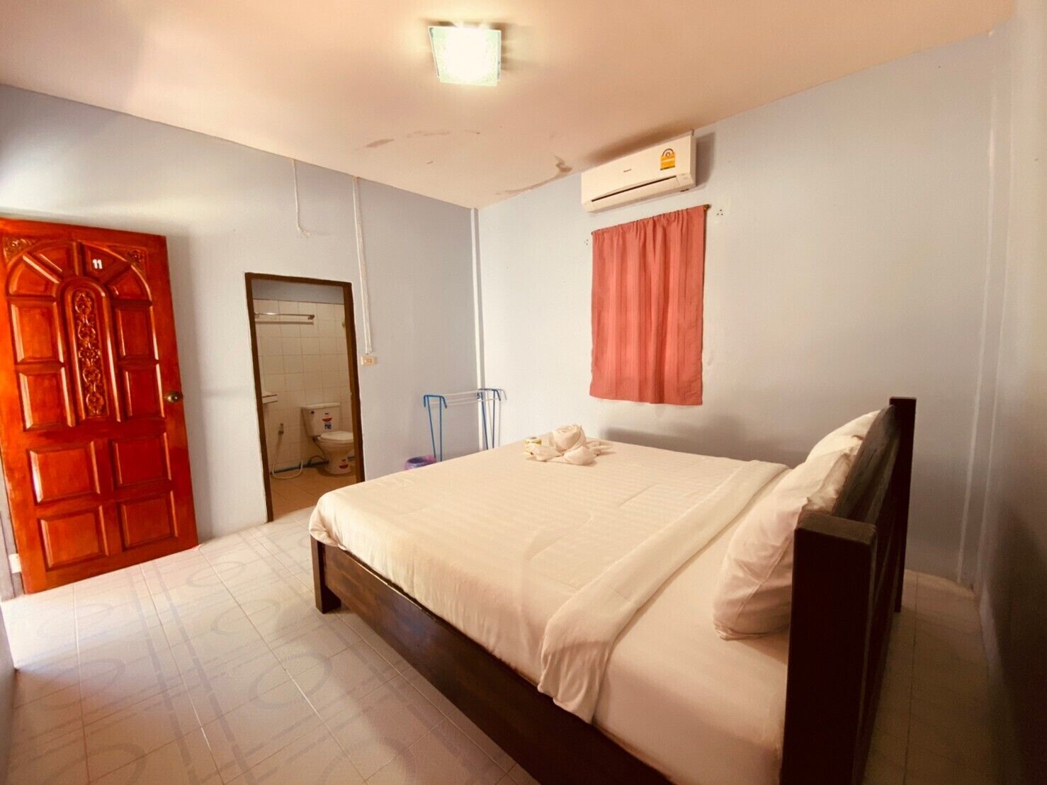 A bedroom with a bed, a door, an air conditioning unit, and a window with a curtain.