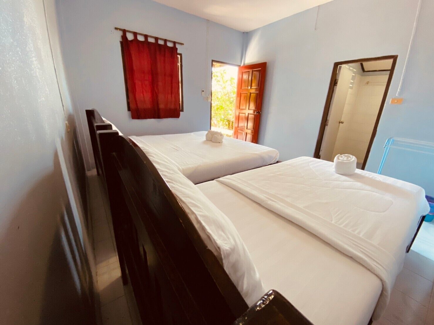A room with two single beds, a wooden headboard, a red curtain, a wooden door, and a mirror.