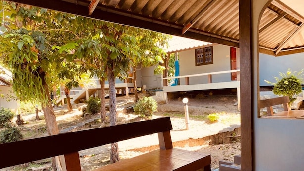 A covered outdoor area with a bench, trees, and a building in the background. - Phupha Bungalow (Ko Pha-ngan)