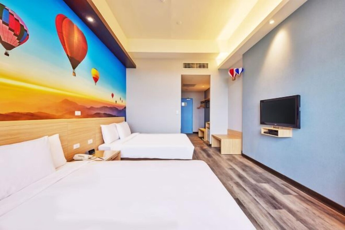 A hotel room with two beds, a TV, and a mural of hot air balloons.