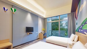 Quarto de hotel com duas camas, uma escrivaninha, uma televisão e uma varanda com vista para o verde.
