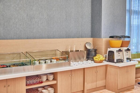 A buffet setup with food containers, a coffee station, and a fruit basket.