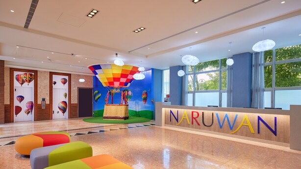 Uma área de recepção com assentos coloridos, um balcão de atendimento e um mural de balões.