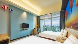 Quarto de hotel com duas camas, televisão, escrivaninha e uma grande janela com vista para a cidade.