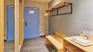 Quarto de hotel com um banco de madeira, uma mesa com pratos e garrafas de água, e duas portas azuis.