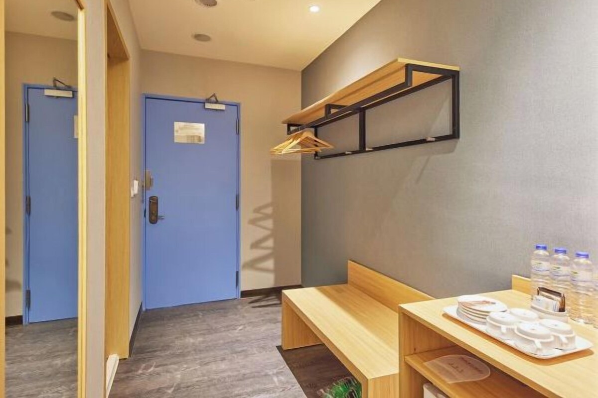 A hotel room with a wooden bench, a small table with plates and water bottles, and a blue door.